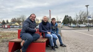 Nauens Bürgermeister Herr Meger und Kollegen aus dem i2030-Team sitzen auf der neuen i2030-Bank vor dem Bahnhof Nauen Bild: Stadt Nauen